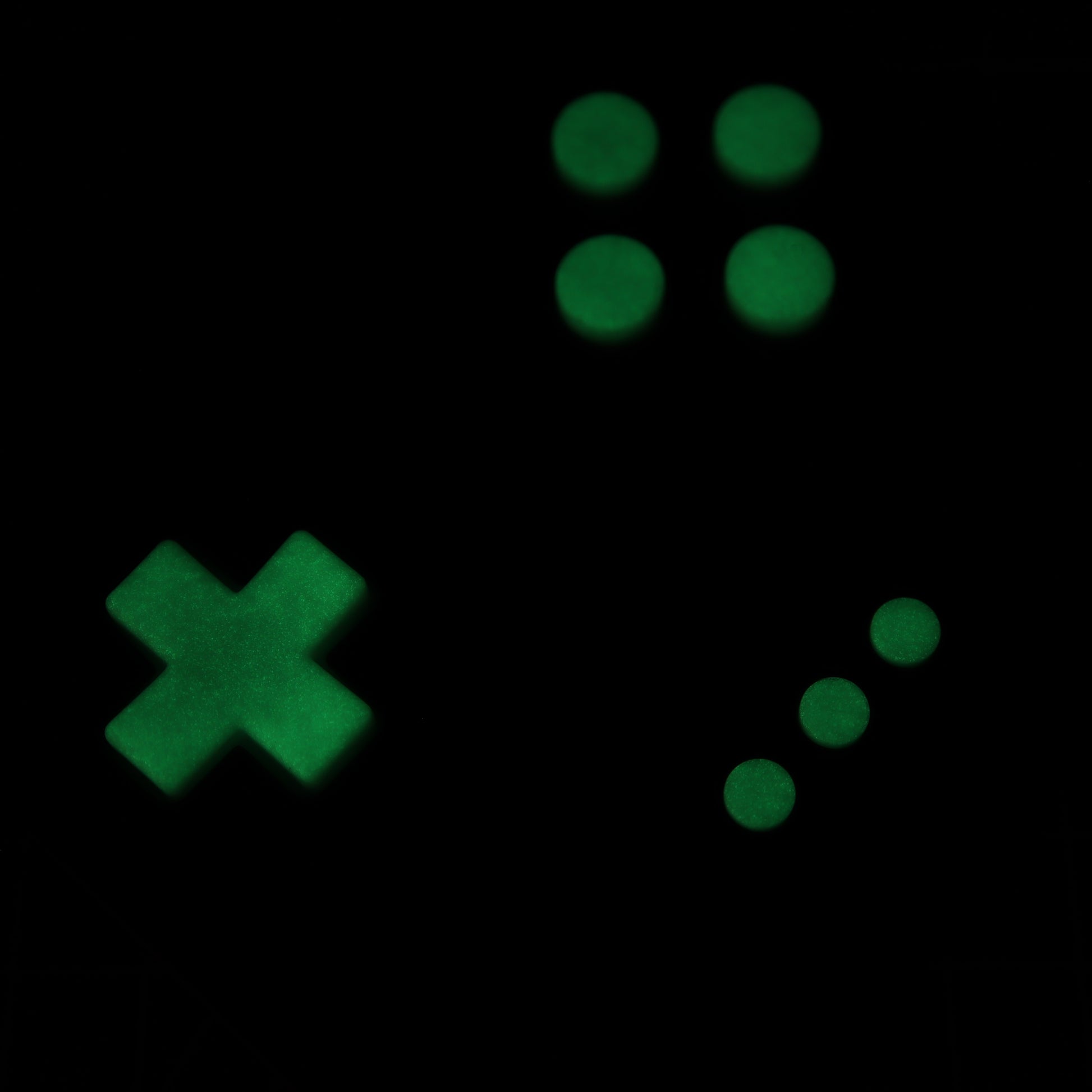 The Analogue Pocket - Custom Button - GITD Green features green glowing symbols on a black background, including an "X" shape, four dots forming a square, and three diagonal dots, reminiscent of handmade molds.