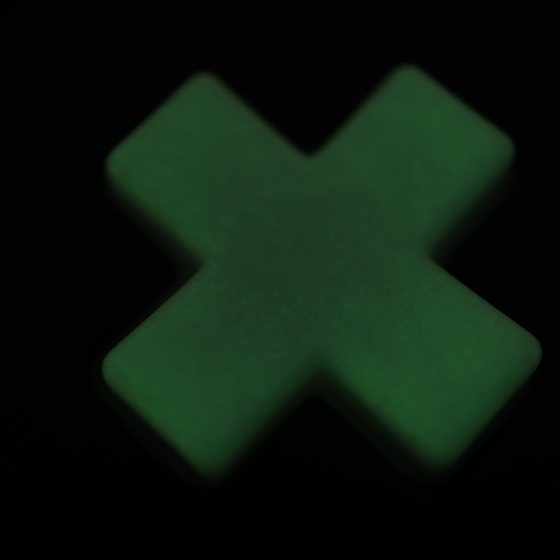 A glowing GITD Green plus sign-shaped object, resembling Analogue Pocket - Custom Button, contrasts sharply against a black background.