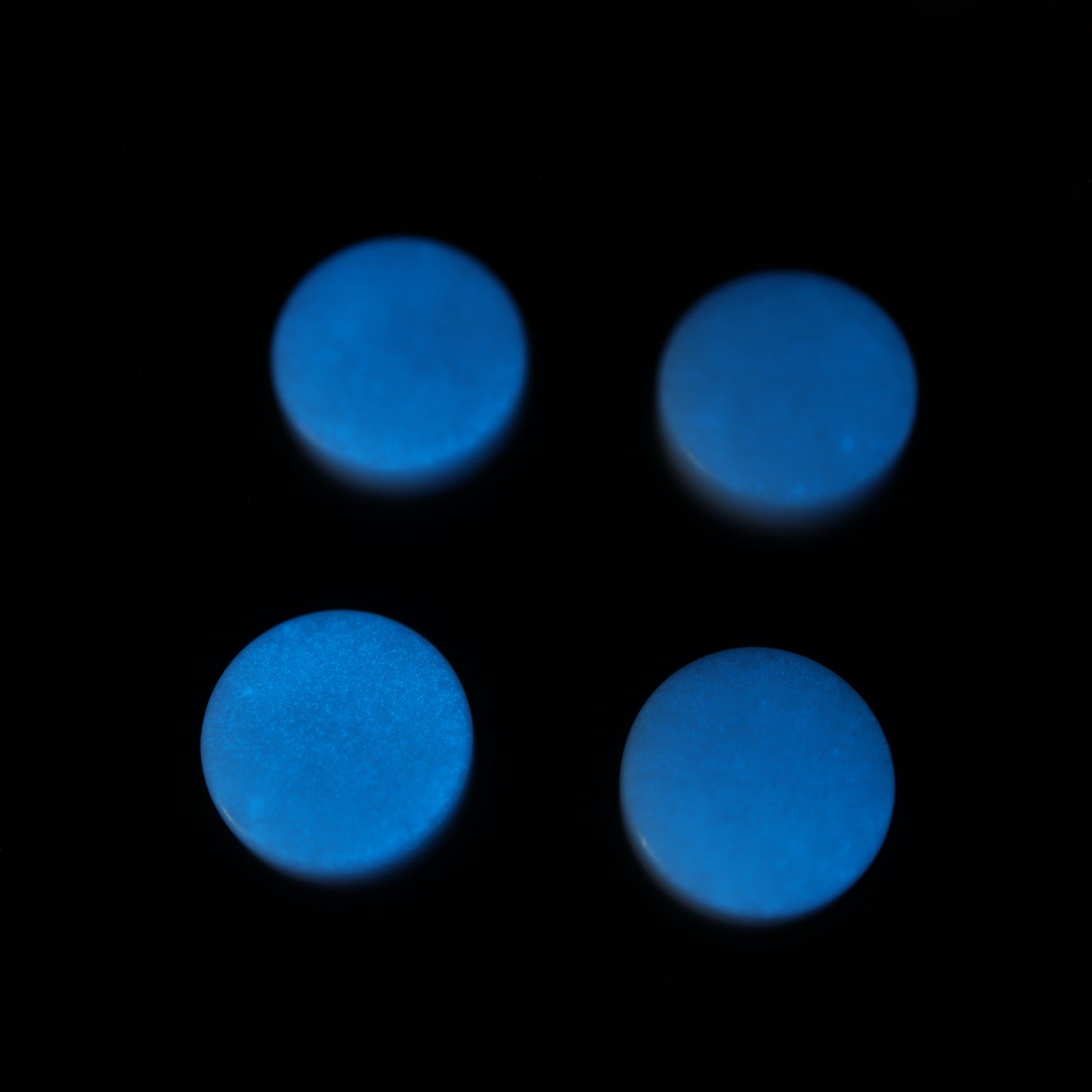 Four Analogue Pocket - Custom Button - GITD Blue circular buttons rest on a black background, reminiscent of handmade molds.