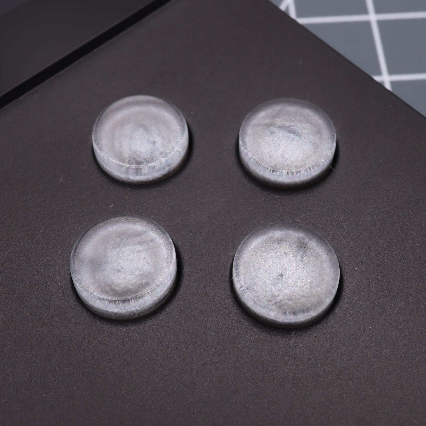Four round, translucent rubber pads, similar to the Analogue Pocket - Custom Button in Metallic Silver, rest on a dark surface.