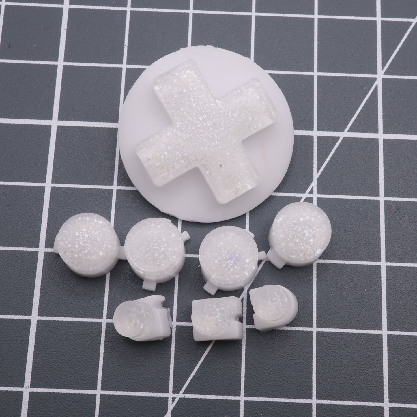 The Pearl White custom button for the Analogue Pocket sparkles gracefully against a gray grid backdrop.