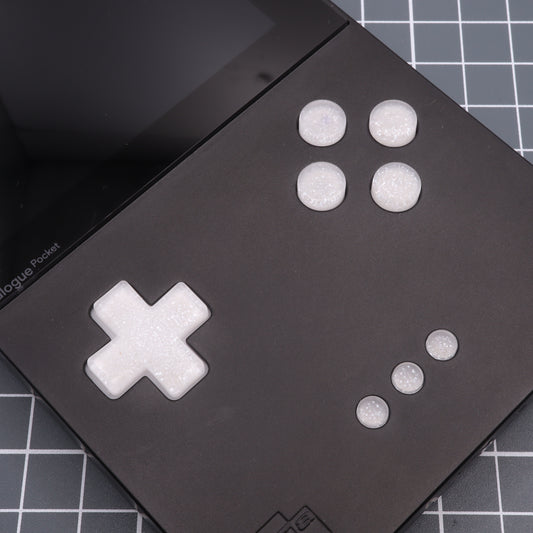 A close-up of the Analogue Pocket - Custom Button - Pearl White showcases custom-cast buttons, a D-pad, and smaller buttons on its grid-patterned surface.