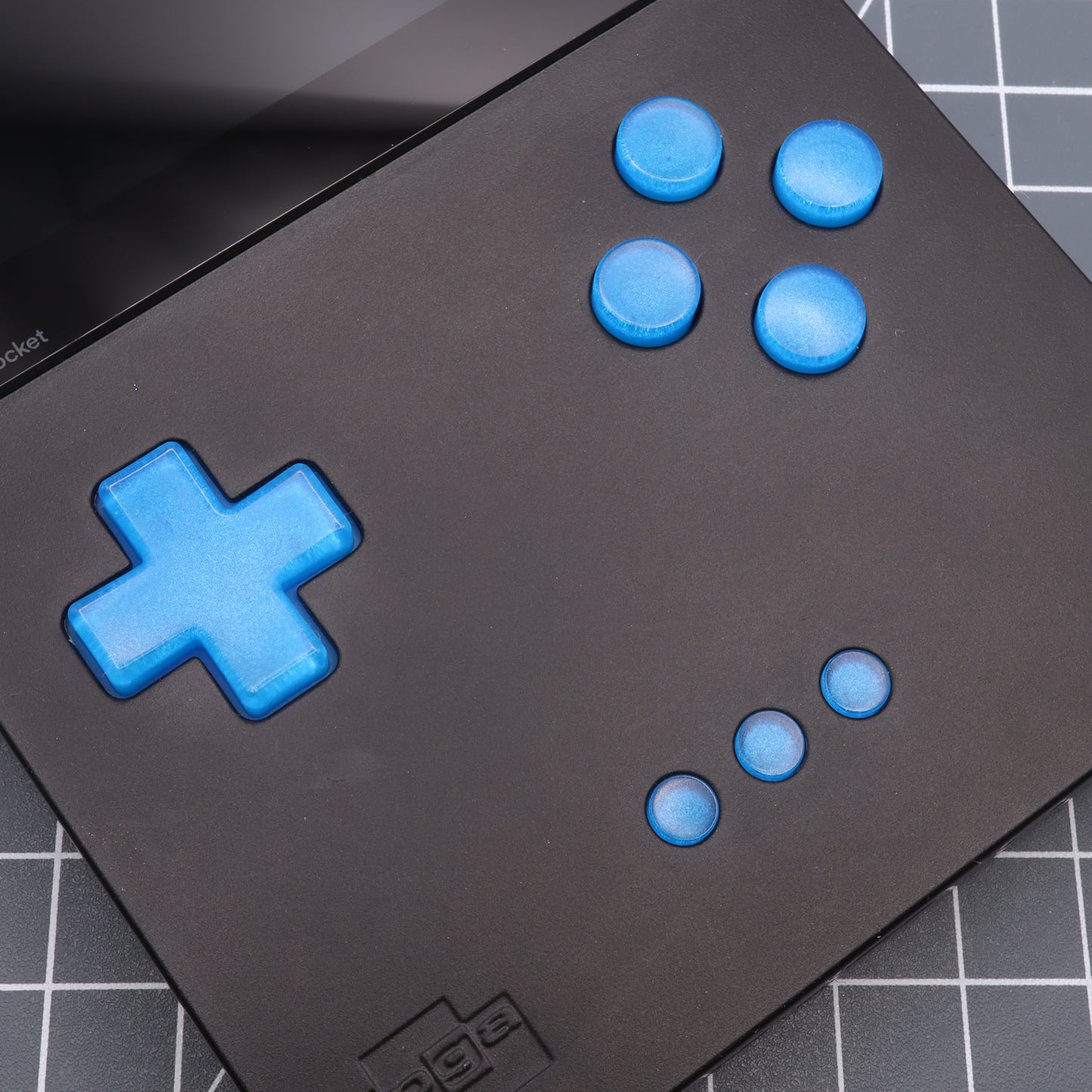 Close-up of an Analogue Pocket with custom Blueberry Candy buttons on a black grid-patterned surface.