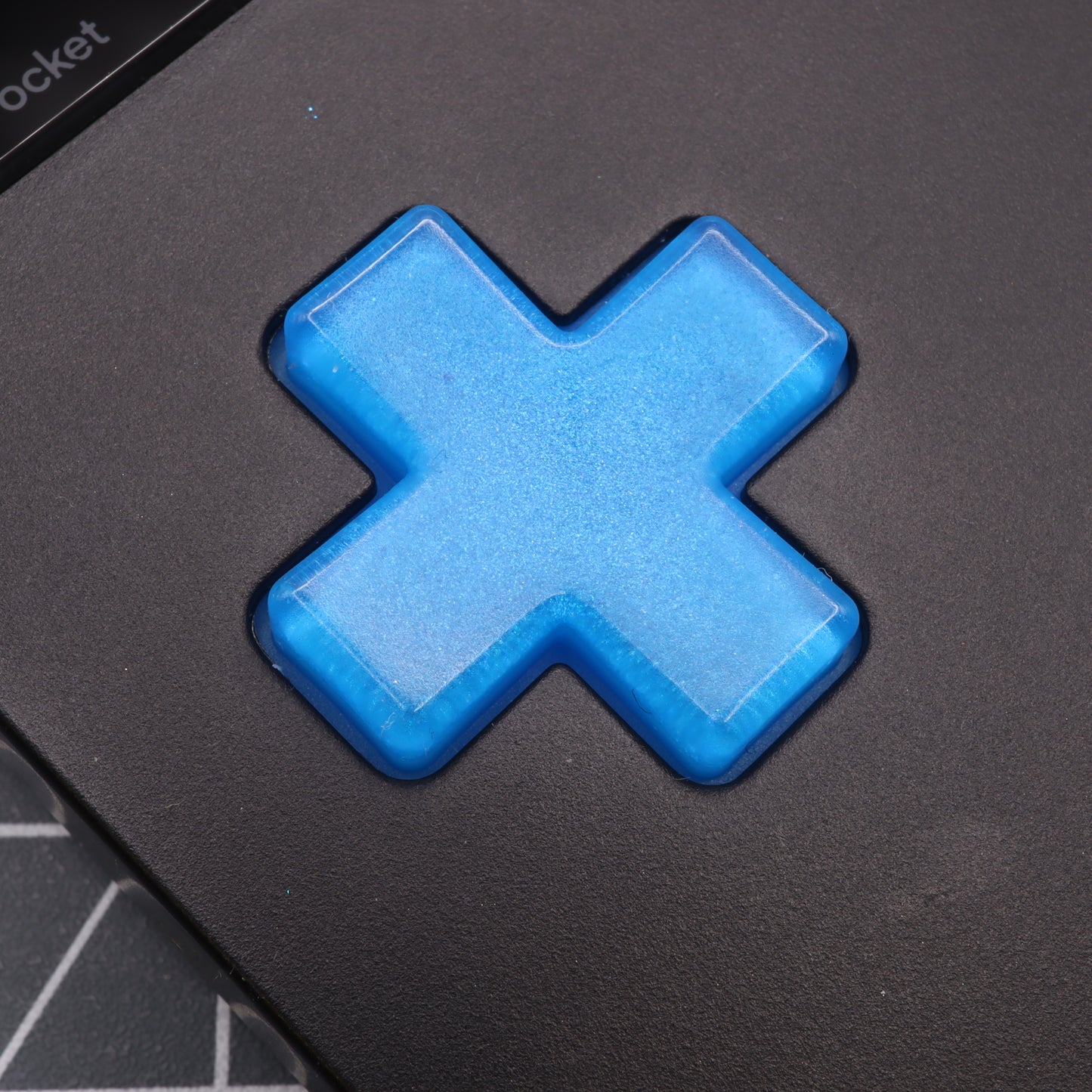 Close-up of the Blueberry Candy cross-shaped button on a black surface, custom-cast with precision using handmade molds for a perfect fit on Analogue Pocket buttons.