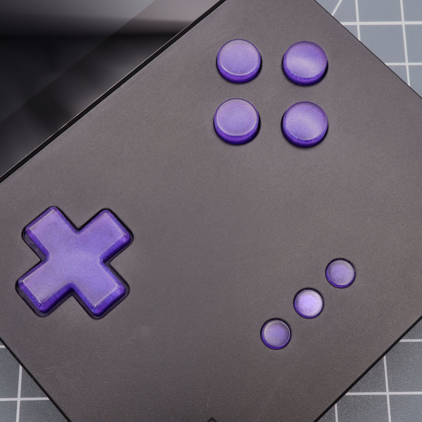 Close-up of a black Analogue Pocket with Grape Candy buttons, showcasing a cross-shaped directional pad and four circular buttons in a grid pattern, crafted using custom-cast molds for precision and style.