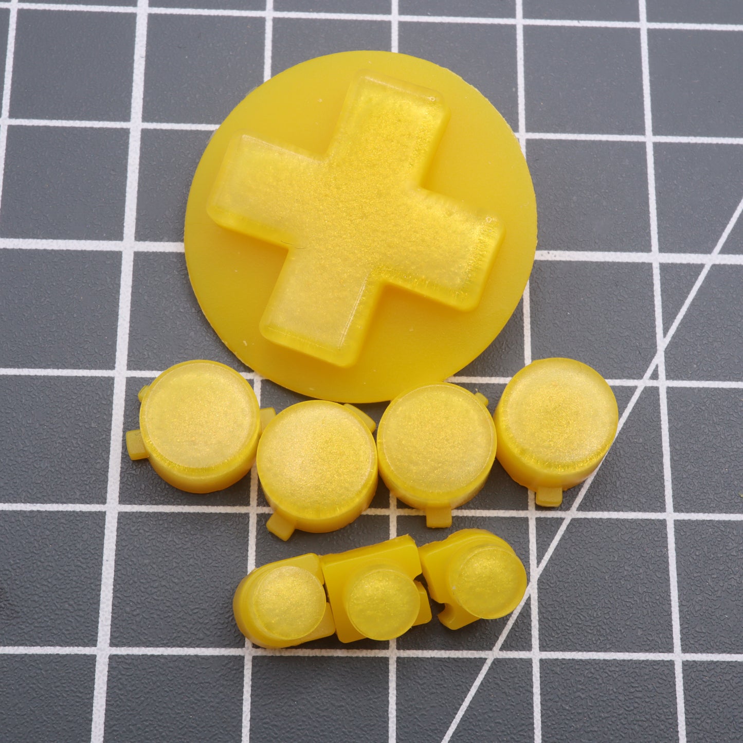 A Lemon Candy yellow plastic D-pad and custom-cast buttons, inspired by the Analogue Pocket, elegantly rest on a gridded surface.