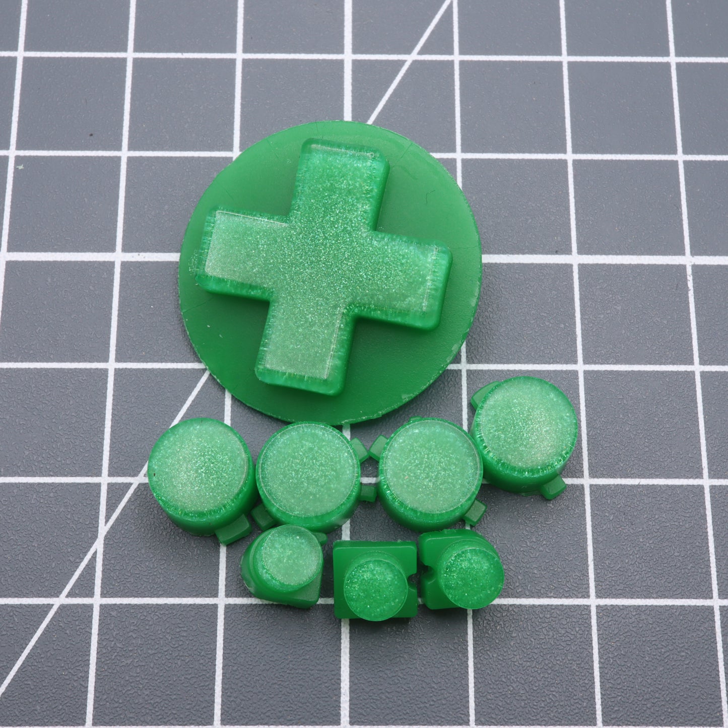 Lime Candy Analogue Pocket features a green plastic cross shape with seven custom-cast buttons perfectly arranged on a grid-patterned surface.