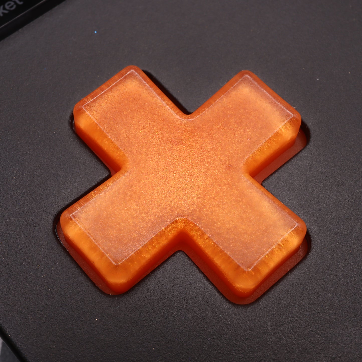 Close-up of an orange, X-shaped object on a dark surface, similar to the Analogue Pocket - Custom Button - Orange Candy.