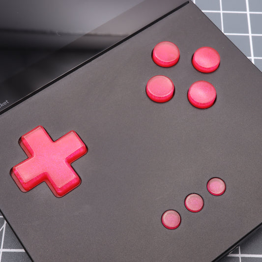 A black Analogue Pocket with Raspberry Candy custom buttons and a red D-pad rests on a grid-patterned surface.