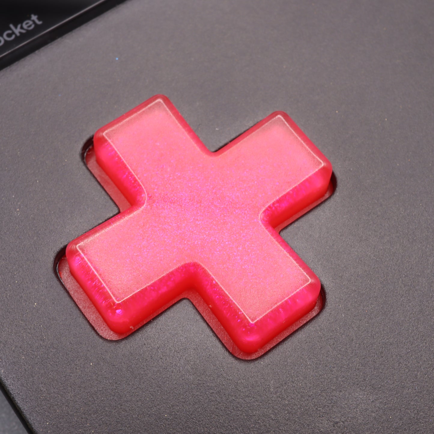 Close-up of a Raspberry Candy Analogue Pocket custom button, crafted from handmade molds, set against a dark surface.