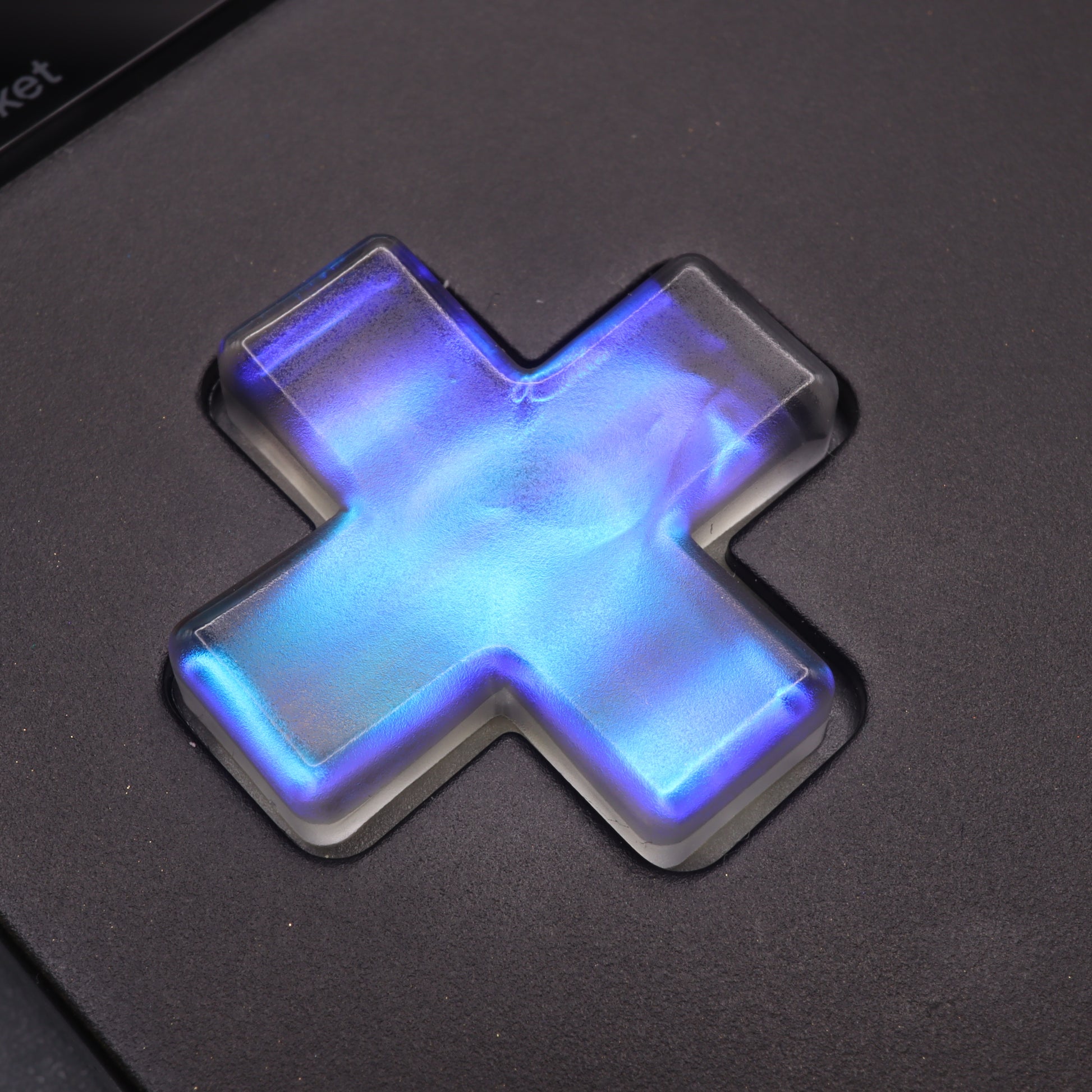 Illuminated Midnight Opal custom-cast button in a blue cross shape on a dark surface.
