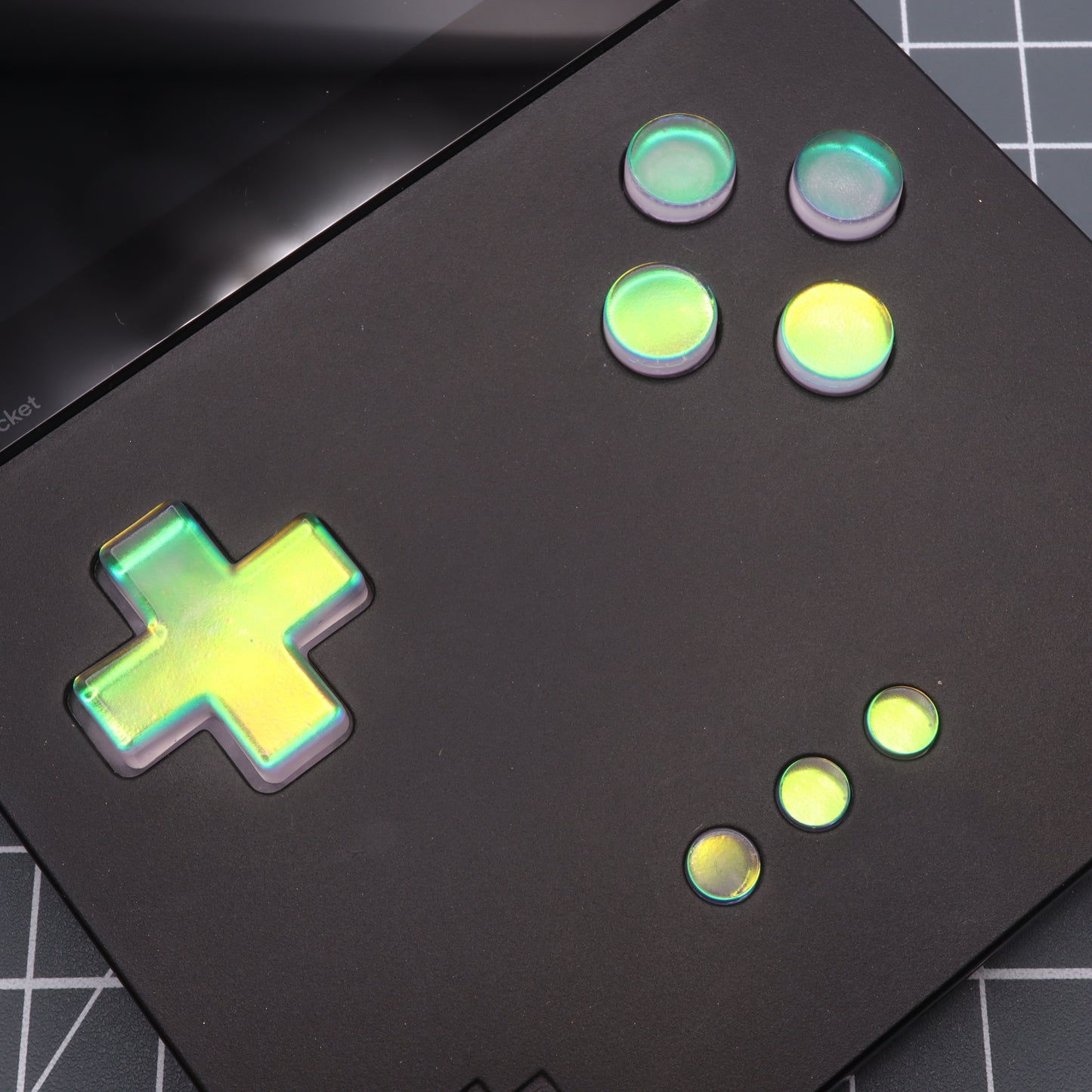 Close-up of the Analogue Pocket with Sunset Opal custom-cast resin buttons and a green D-pad, resting on a grid-patterned surface.