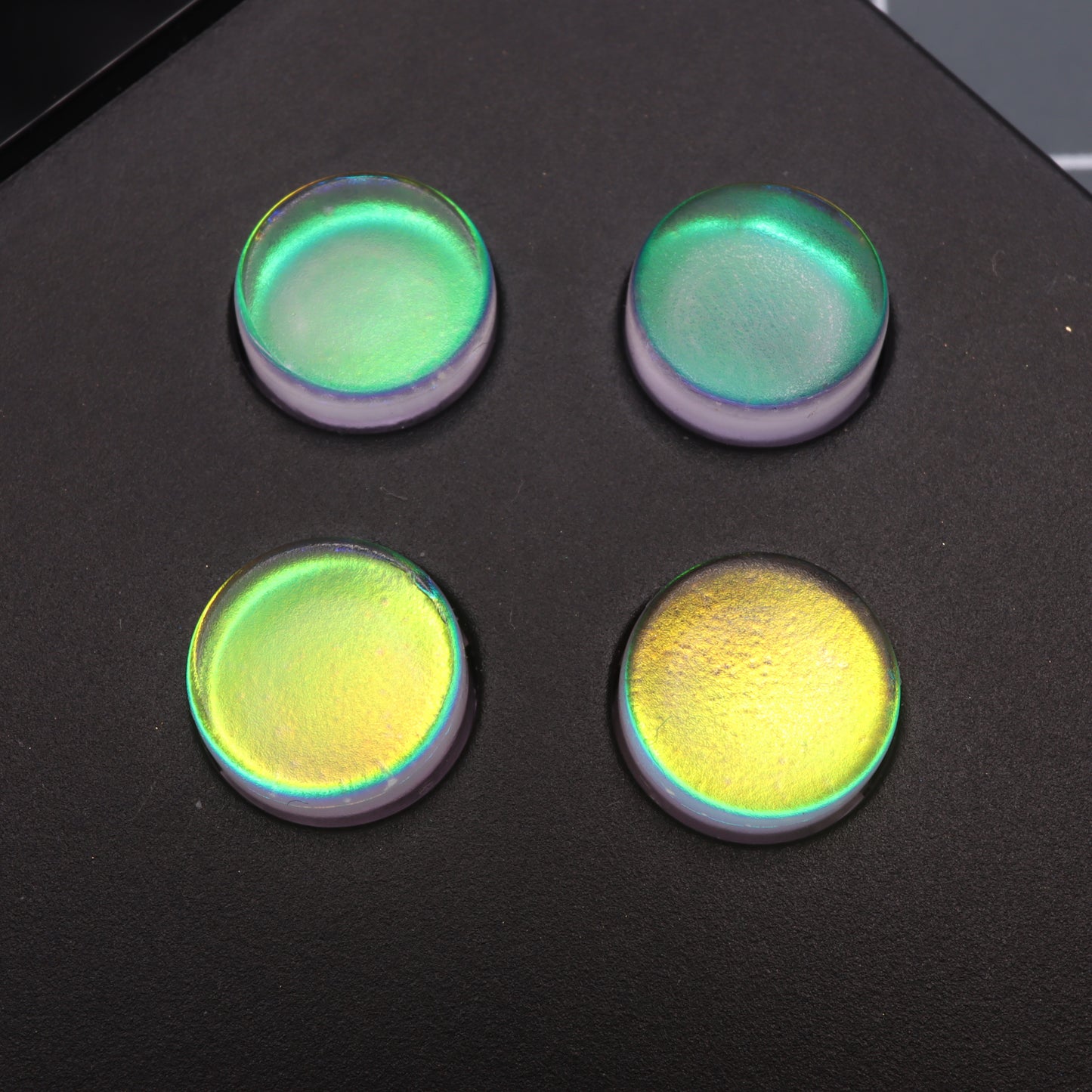 Four round, iridescent Sunset Opal custom buttons for Analogue Pocket on a black surface display a gradient of green to yellow hues.