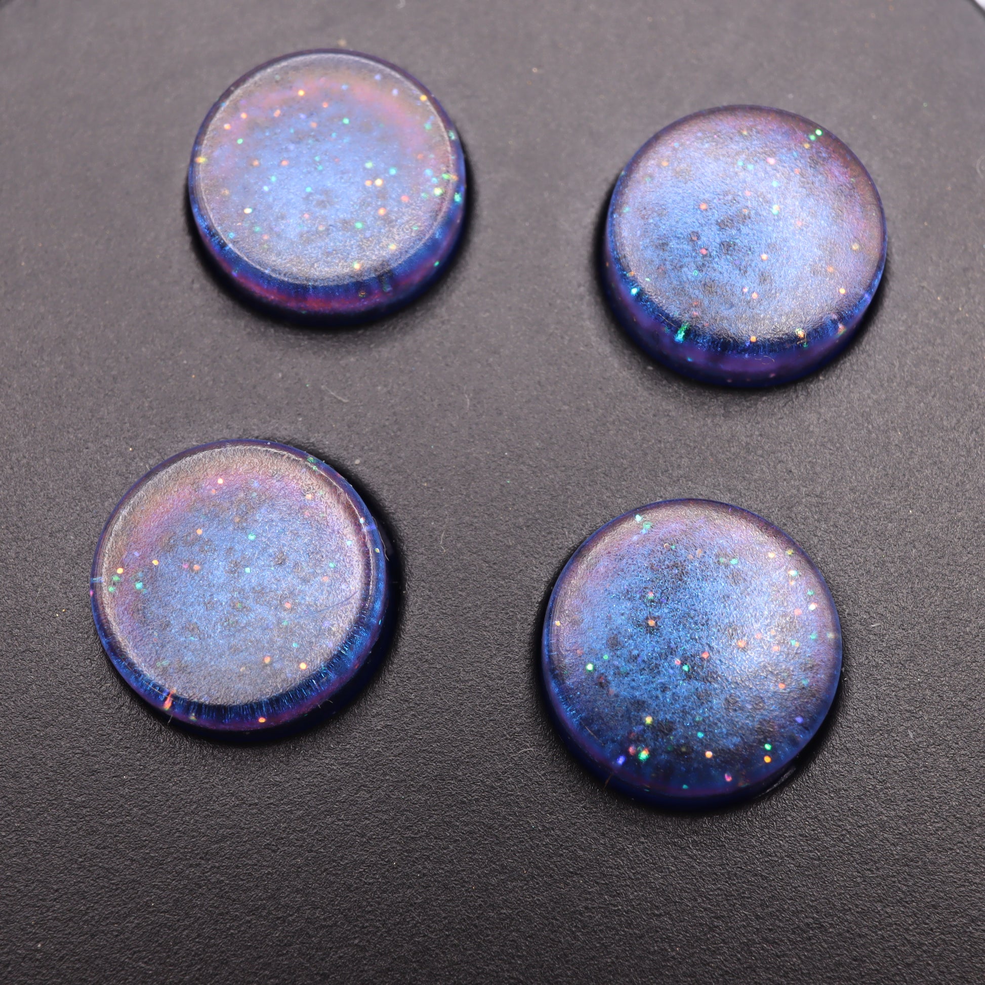 Four Cosmic Blue custom buttons, crafted from handmade molds and arranged on a dark surface, shimmer brilliantly.