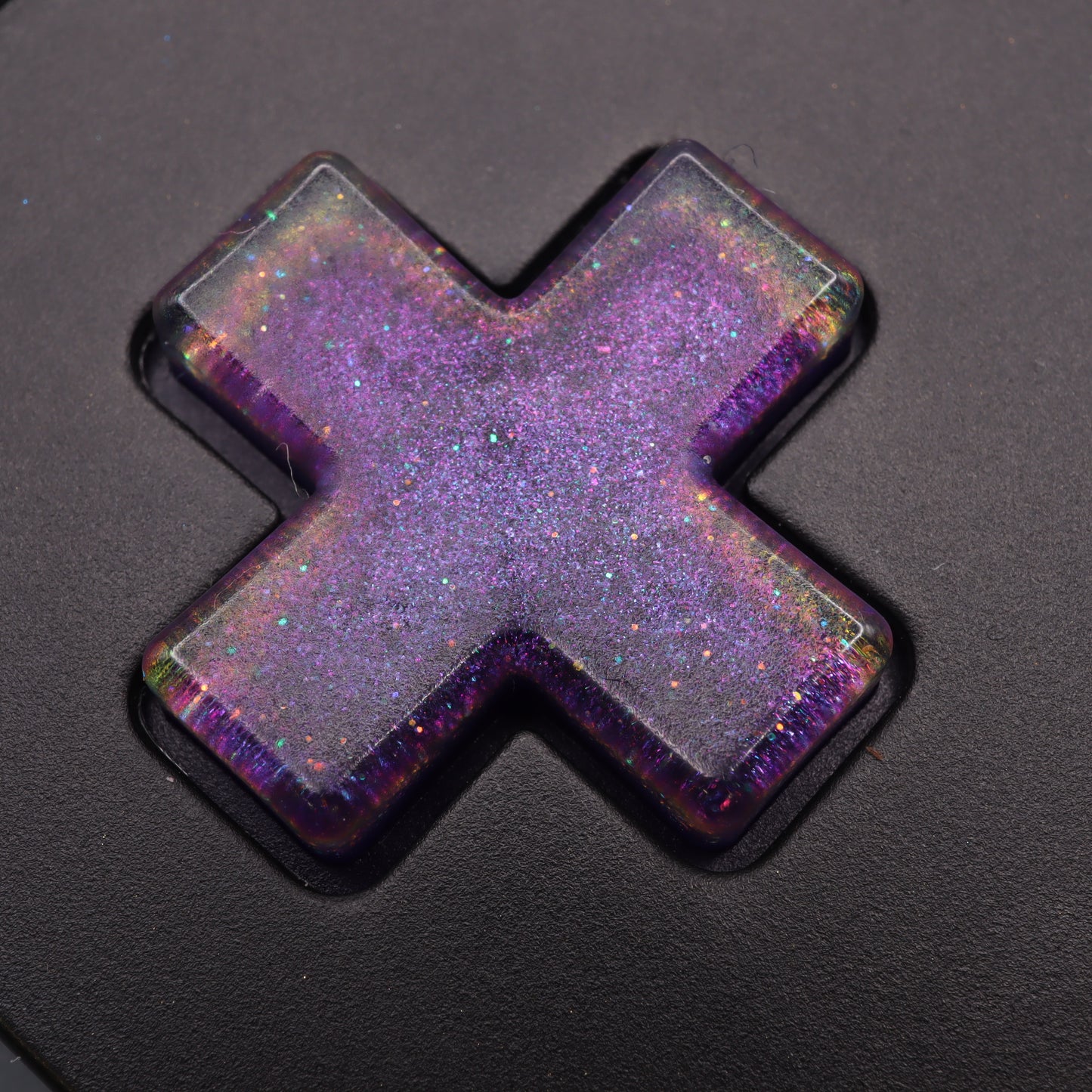 The Analogue Pocket's black keyboard is adorned with a cosmic purple, glittery resin cap featuring an X shape, echoing the charm of custom-cast buttons.