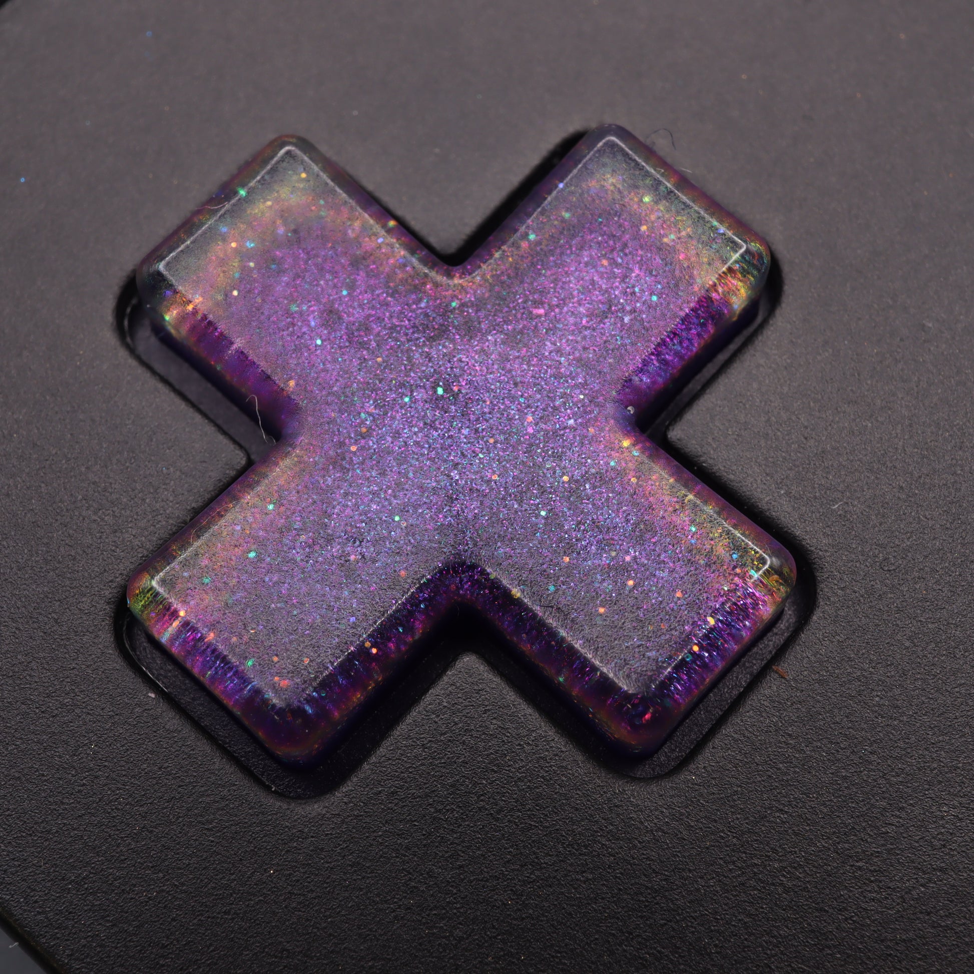 The Analogue Pocket's black keyboard is adorned with a cosmic purple, glittery resin cap featuring an X shape, echoing the charm of custom-cast buttons.