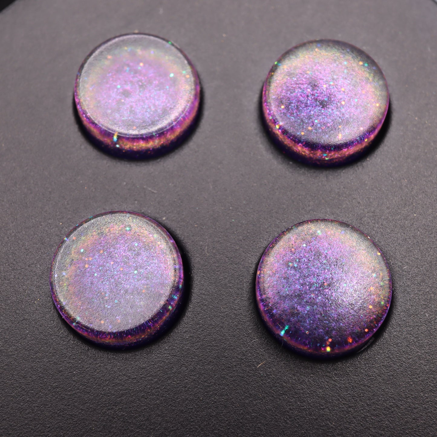 Four round, glossy, purple buttons with iridescent sparkles on a dark surface resemble the Analogue Pocket's Cosmic Purple custom-cast buttons.