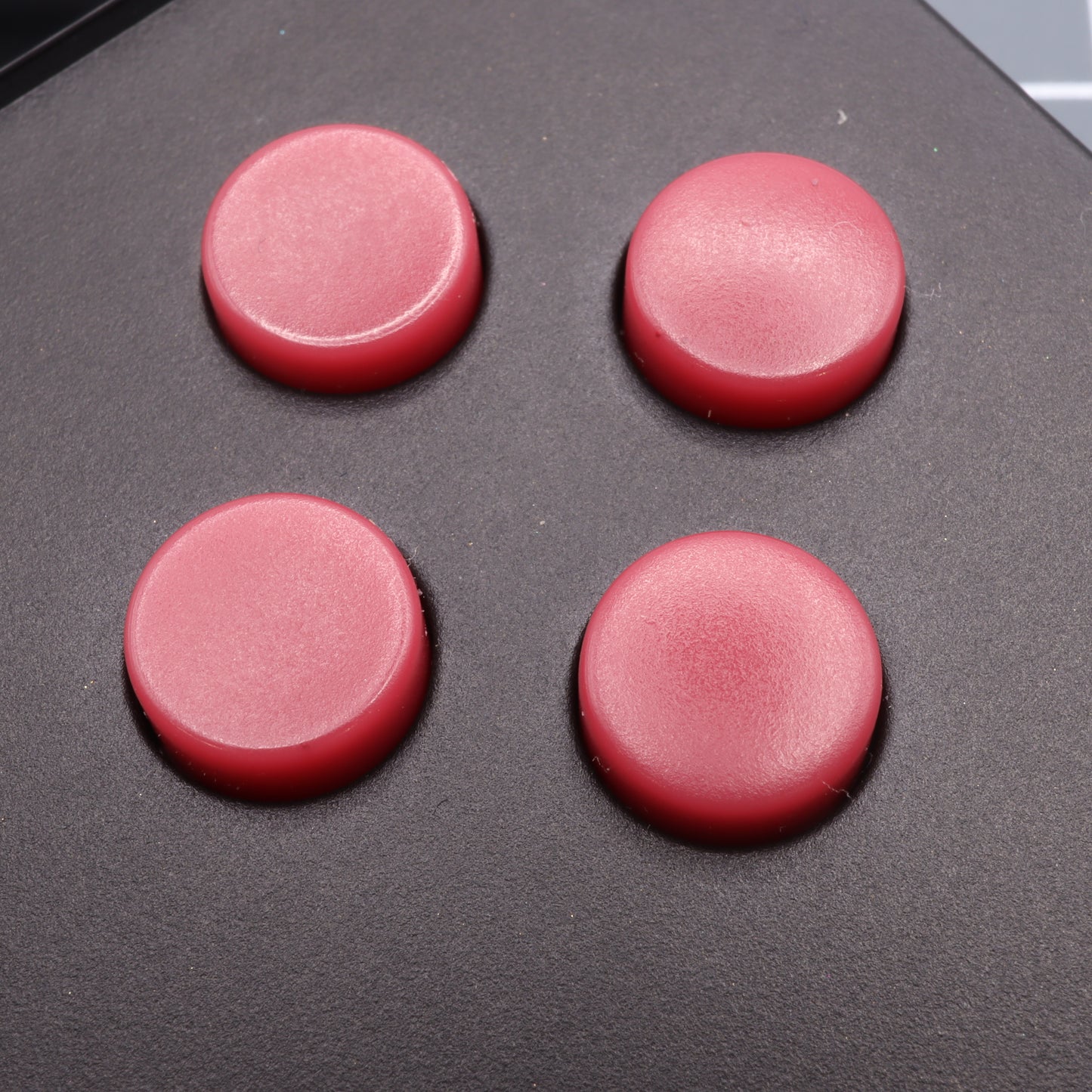 Four Game Boy DMG style, red circular buttons, crafted using handmade molds, are elegantly displayed on a sleek black surface.