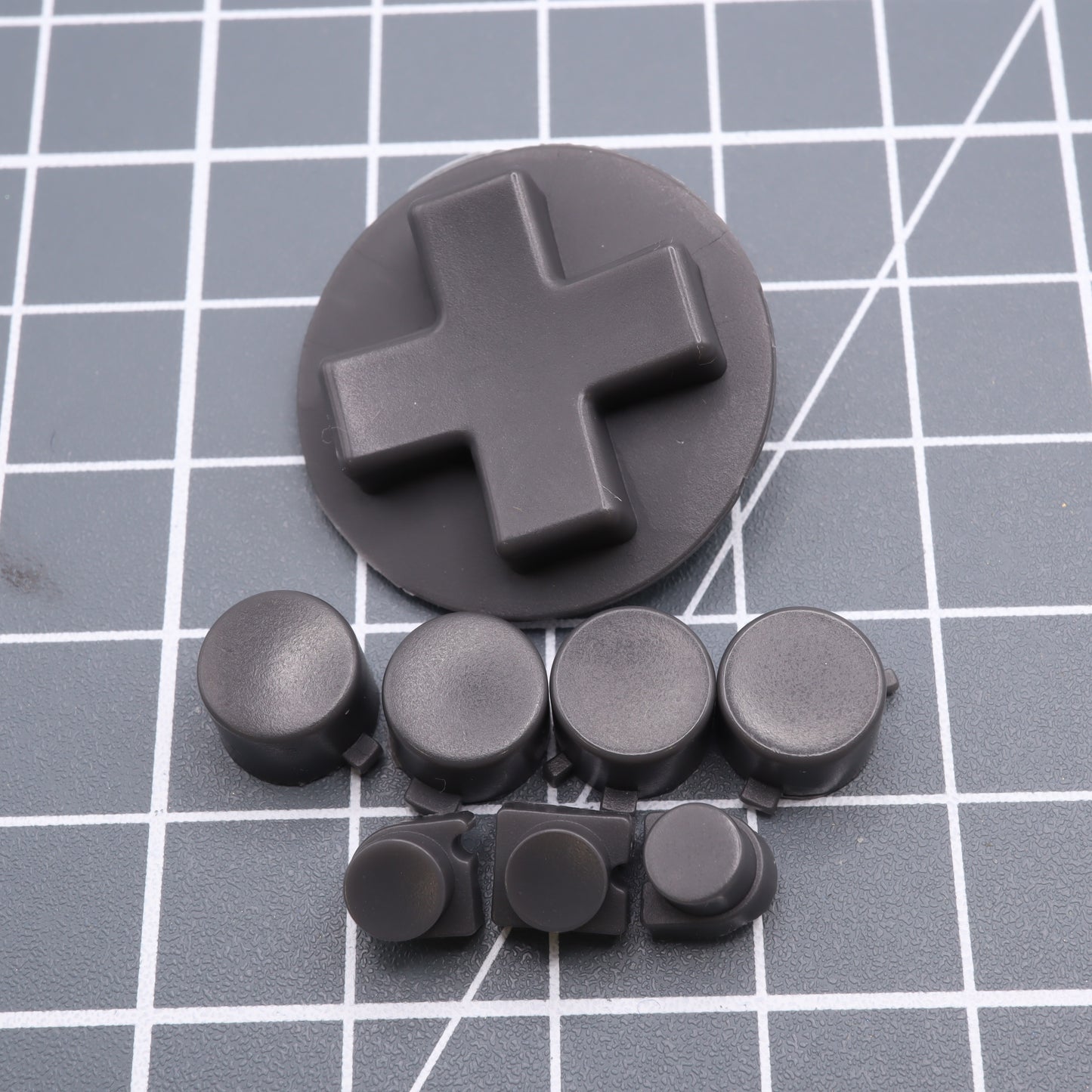 The Analogue Pocket - Custom Button - DMG Play it Loud Style features a black D-pad and custom-cast buttons set against a gray grid background.