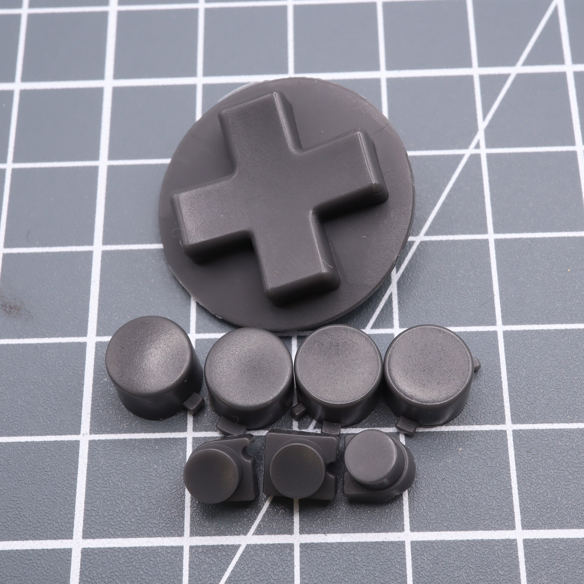 The Analogue Pocket - Custom Button - DMG Play it Loud Style features a black D-pad and custom-cast buttons set against a gray grid background.