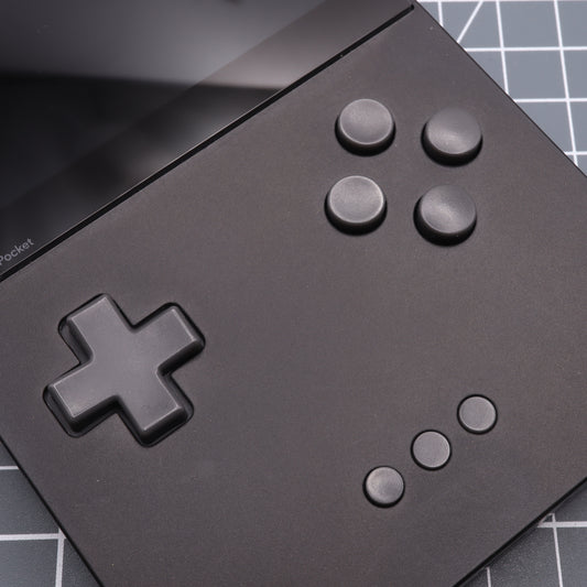 Close-up of the Analogue Pocket - Custom Button - DMG Play it Loud Style, a black handheld gaming device with resin buttons, a screen, directional pad, and six circular buttons on a grid-patterned background.