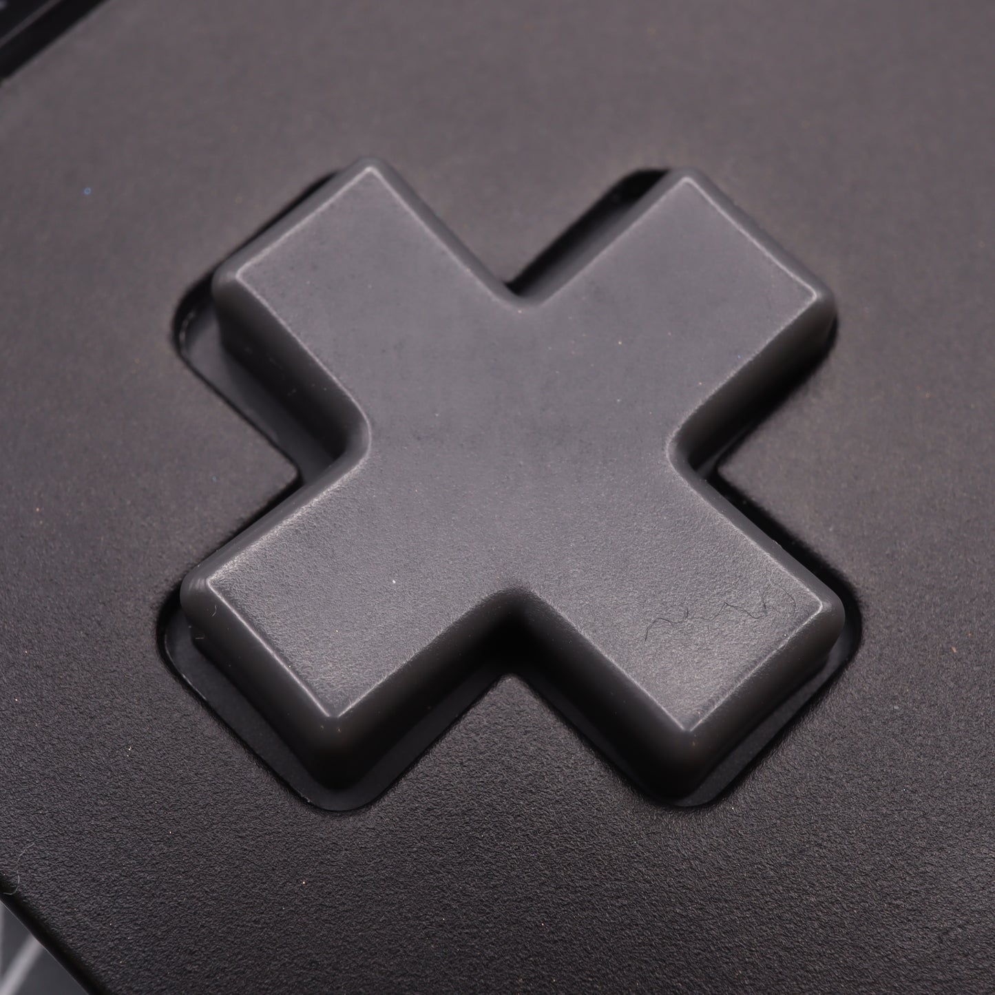 Close-up of an Analogue Pocket - Custom Button in DMG Play it Loud Style, featuring a gray, cross-shaped design on a black surface.