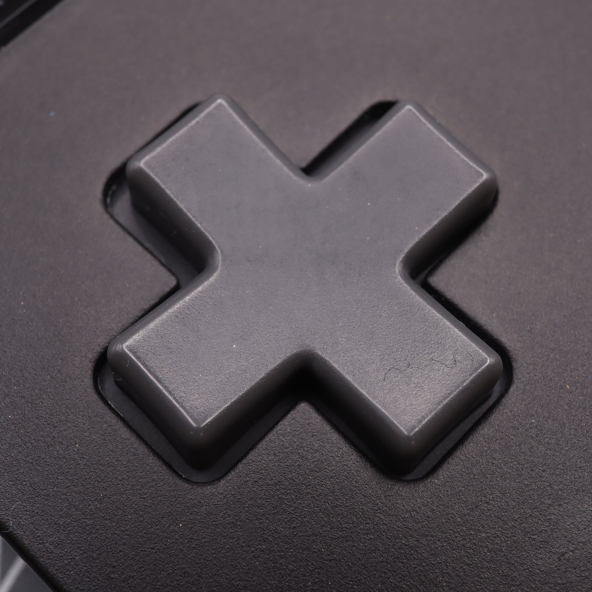 Close-up of an Analogue Pocket - Custom Button in DMG Play it Loud Style, featuring a gray, cross-shaped design on a black surface.