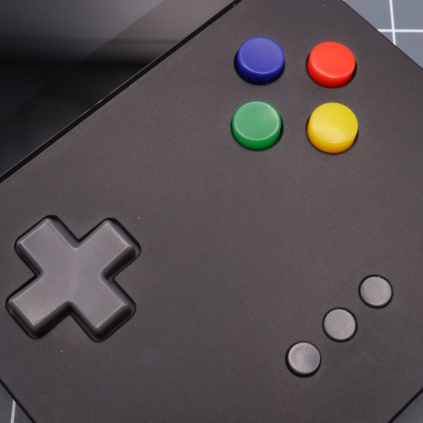 Close-up of the Analogue Pocket - Custom Button - SNES Style, a black gaming controller with custom-cast buttons and a directional pad, featuring vibrant blue, red, green, and yellow accents.