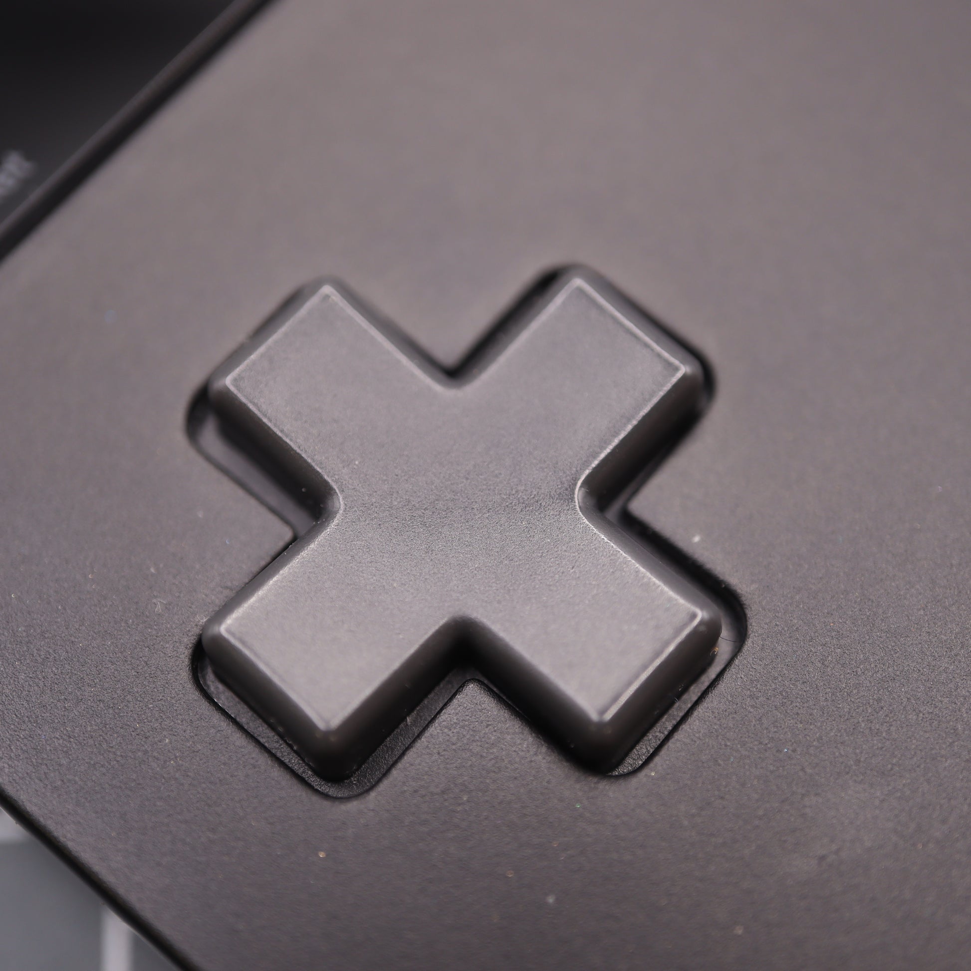 Close-up of a black cross-shaped button on an electronic device, reminiscent of the Analogue Pocket - Custom Button - Famicon Style.