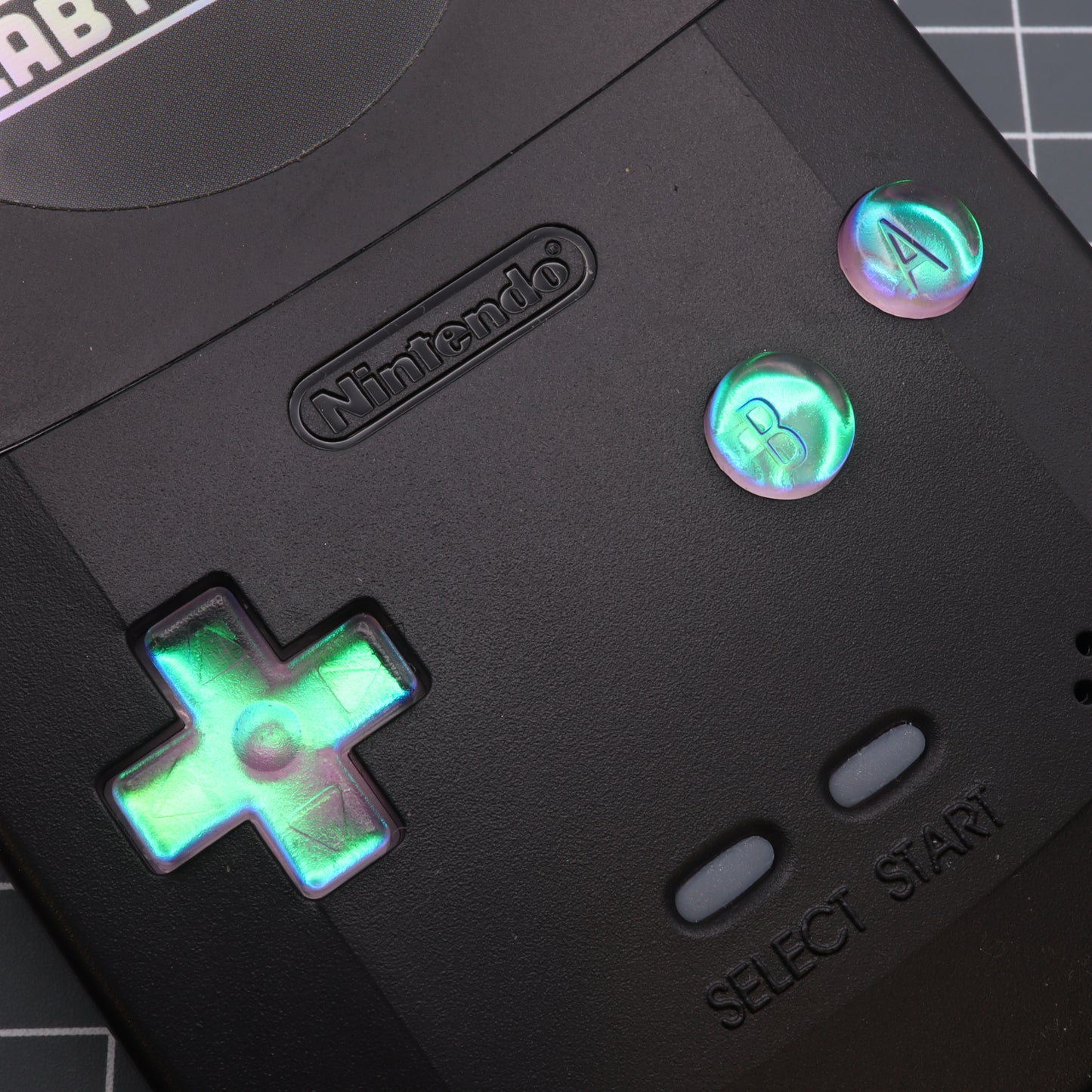 A black labfifteen Game Boy Color - Custom Button - Cool Opal is sitting on top of a table.