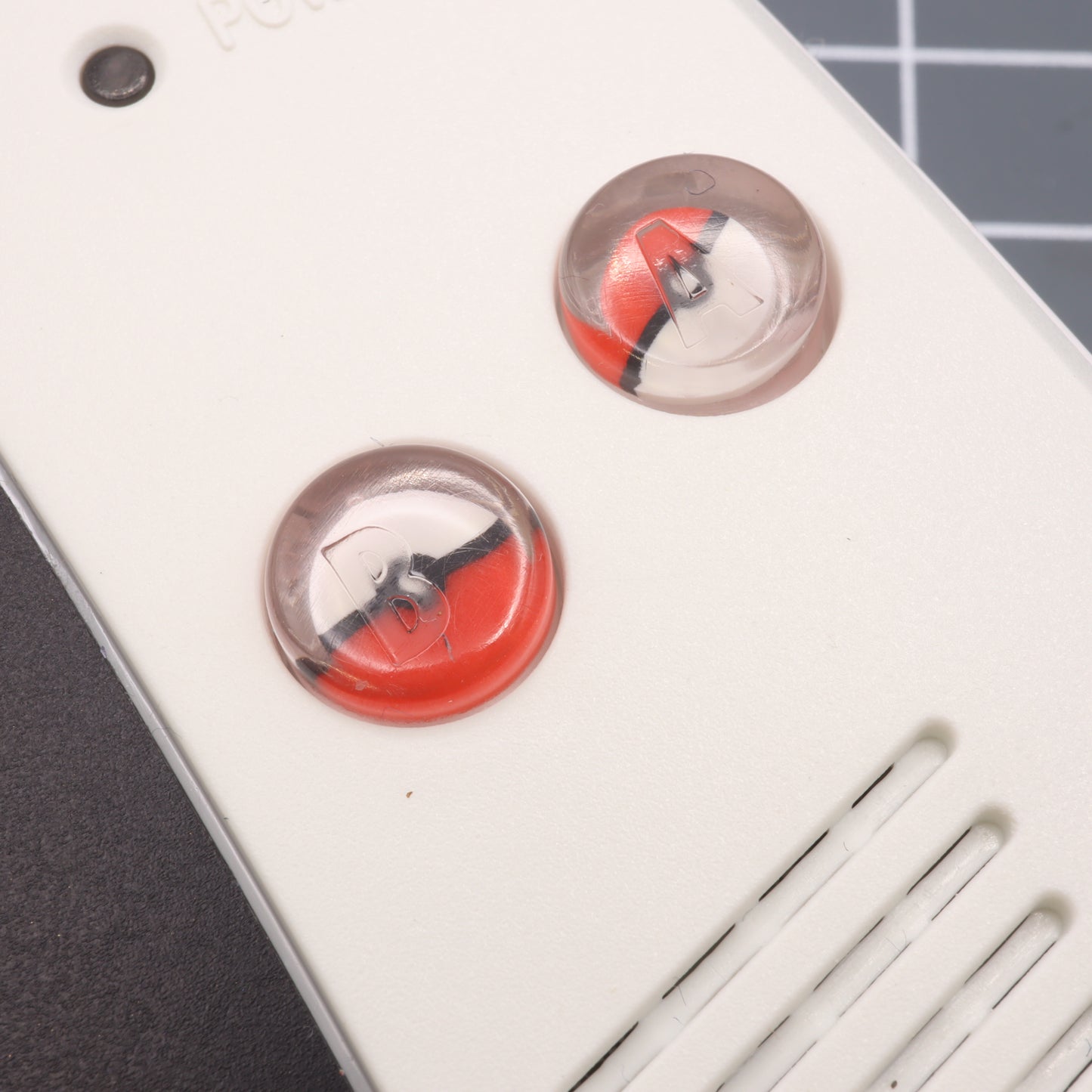 A close up of a white remote with labfifteen's Game Boy Advance - Custom Buttons - Pokeball.