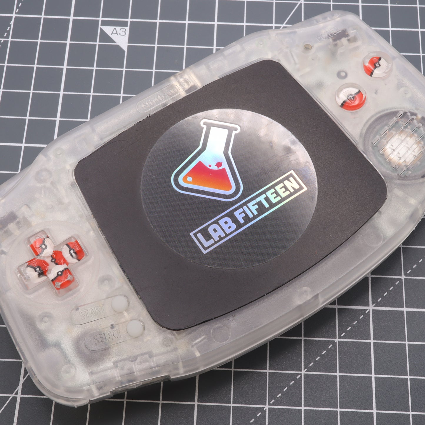 A close up of a labfifteen Game Boy Advance controller with custom Pokeball buttons.