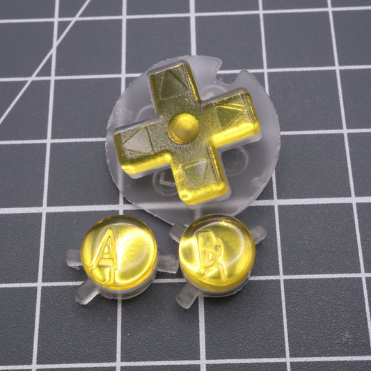 Game Boy Color buttons with lab fifteen co silver chrome gold yellow custom buttons on a table.