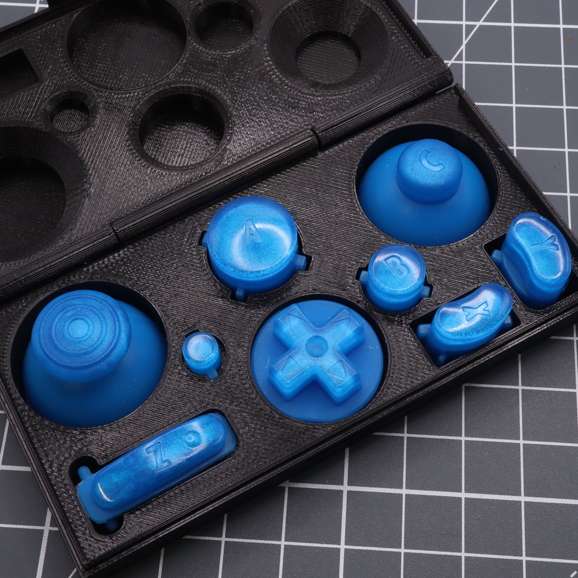 A set of blue silicone molds for GameCube - Custom Button - Blueberry Candy displayed on a black case with compartments.