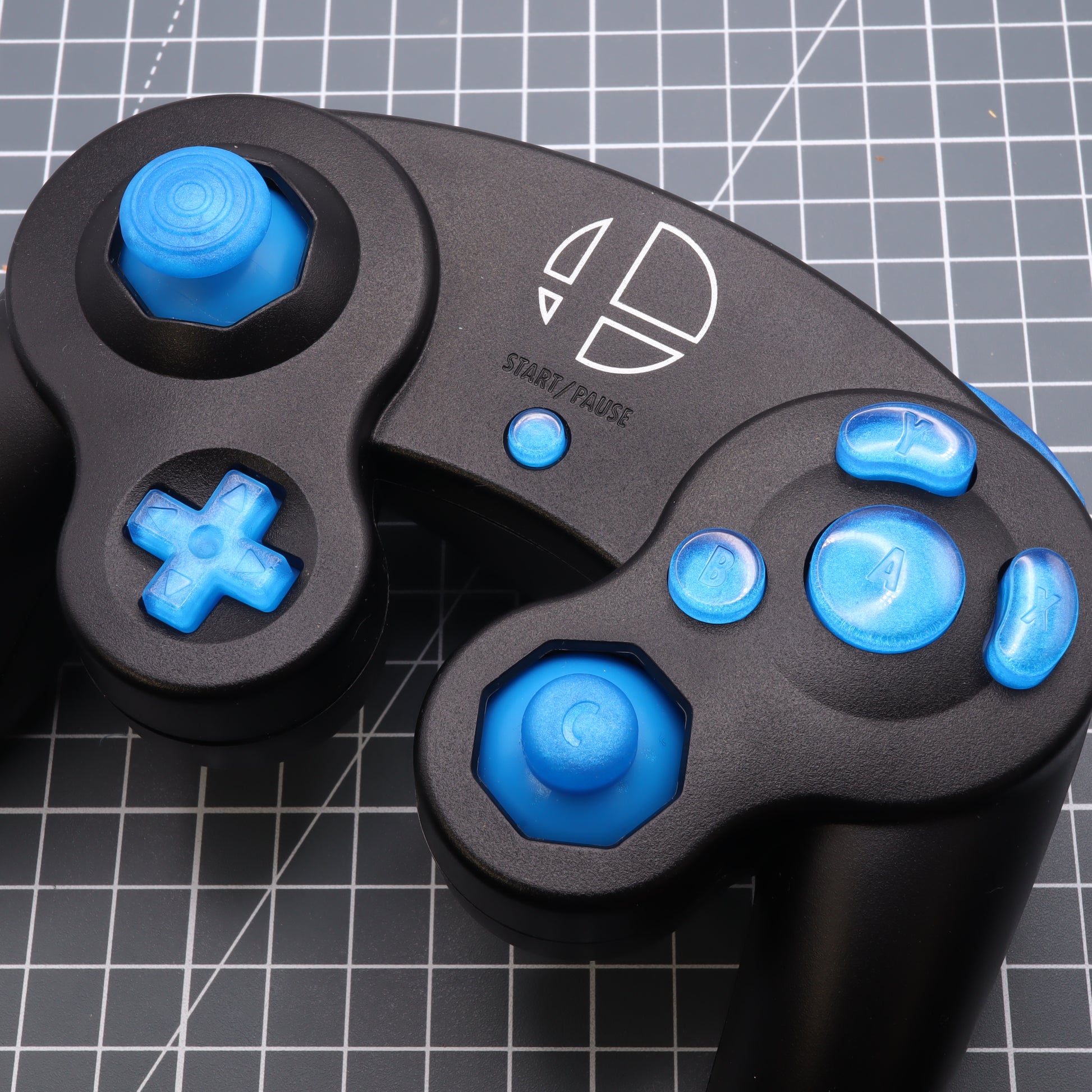 Black and blue game controller with custom-cast GameCube - Custom Button - Blueberry Candy buttons on a grid surface.