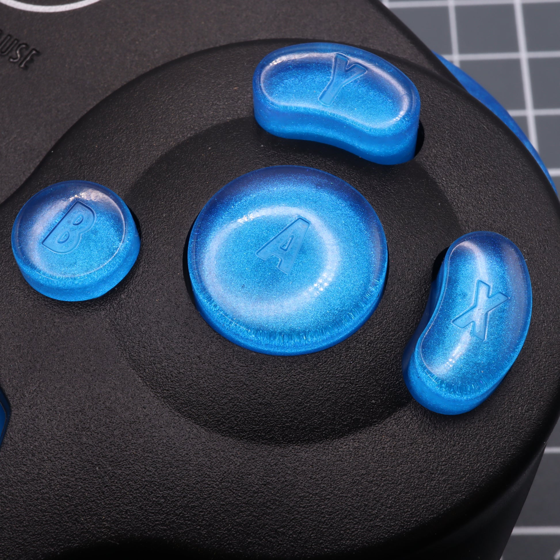 Close-up of the blue GameCube - Custom Button - Blueberry Candy custom-cast resin buttons on a black Nintendo Game Cube controller.