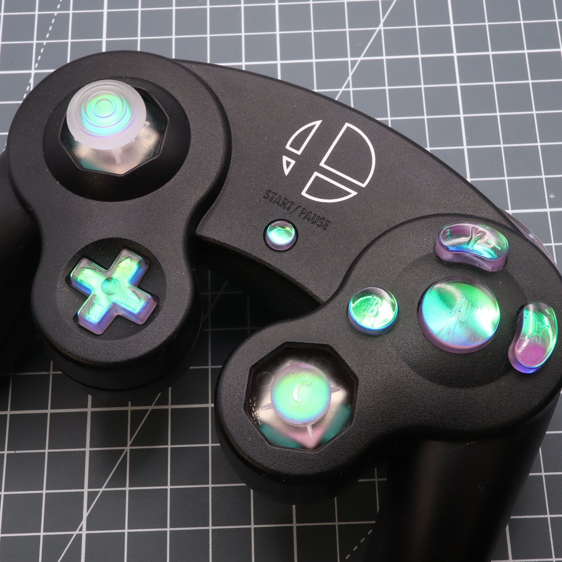 Close-up of a black GameCube controller with Cool Opal custom buttons, analog sticks, and a dichroic effect.