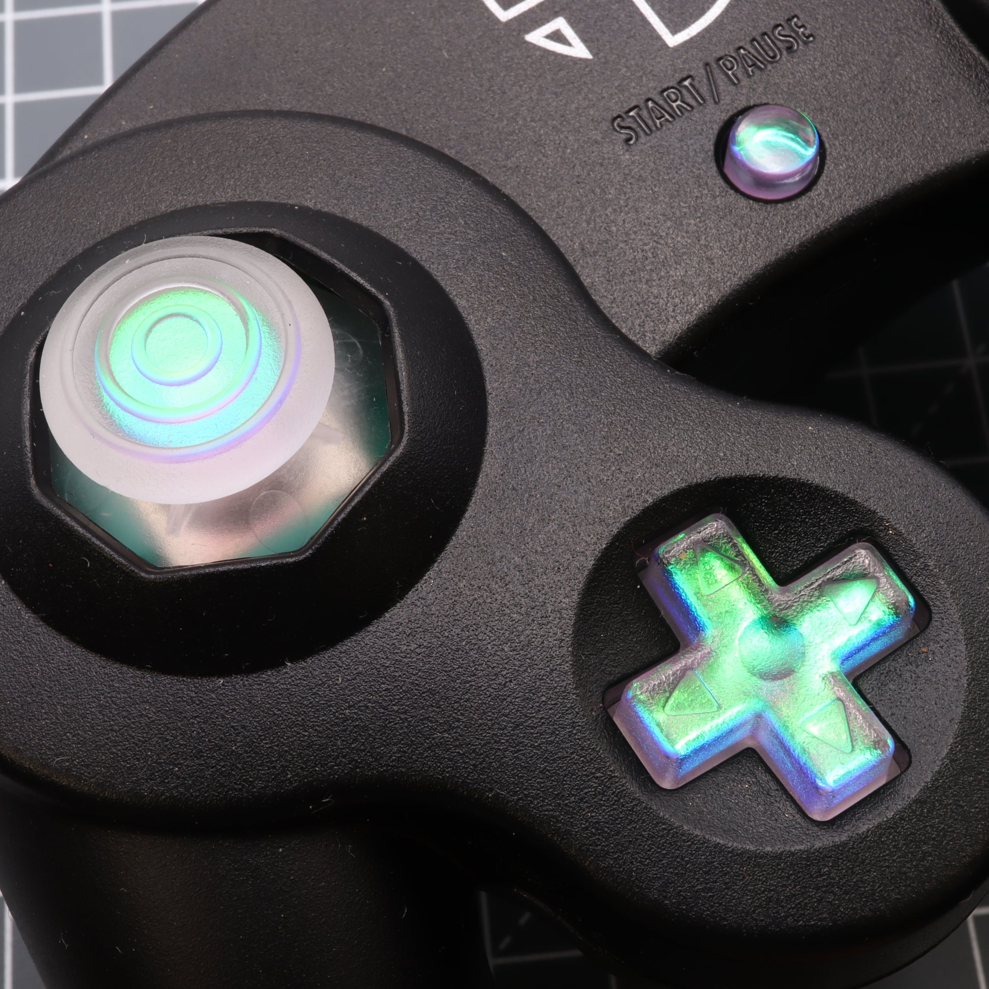 Close-up of a GameCube controller with an illuminated analog stick and a green, glowing dichroic effect.