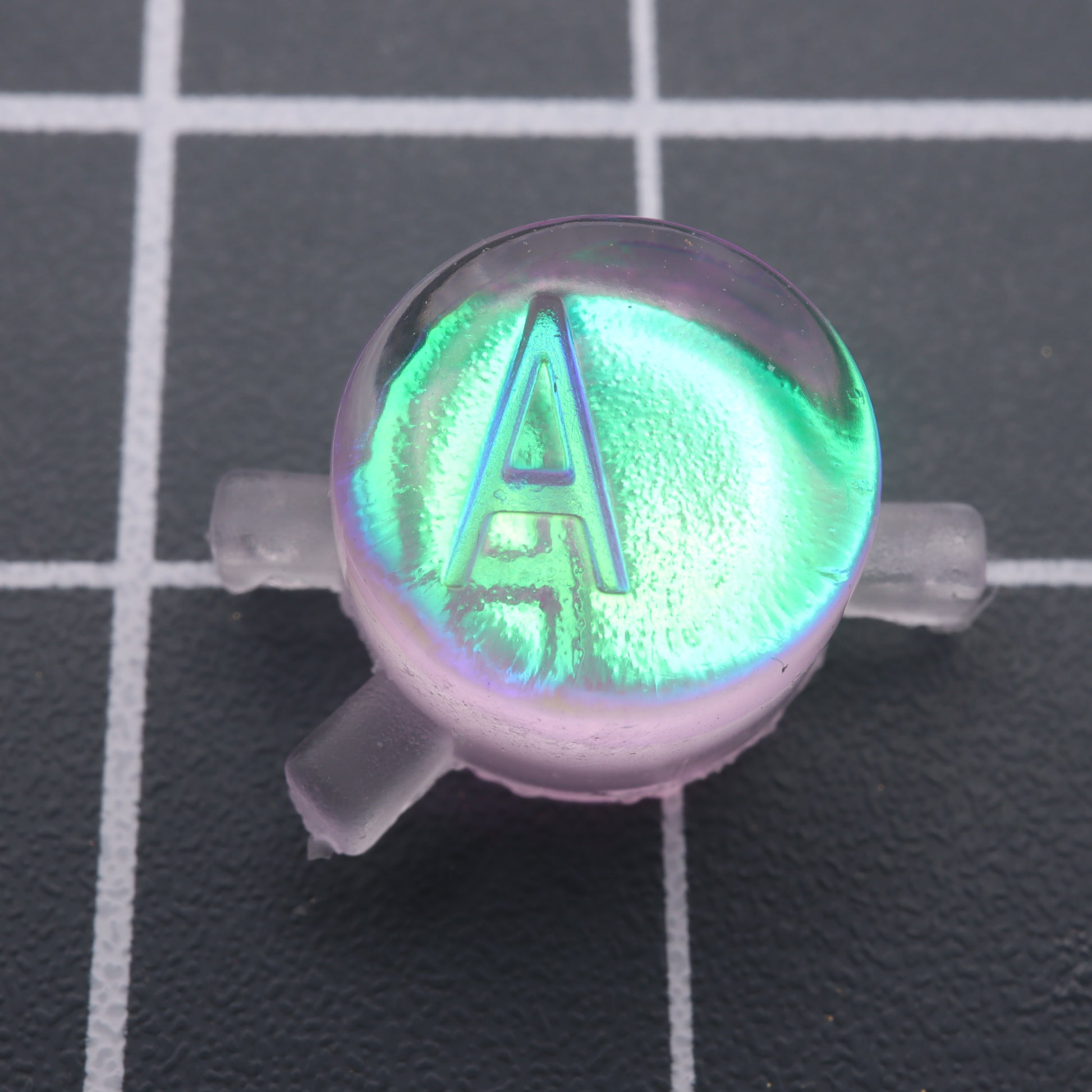 A green and purple glow in the dark resin Game Boy Color - Custom Button - Cool Opal on top of a grid by labfifteen.