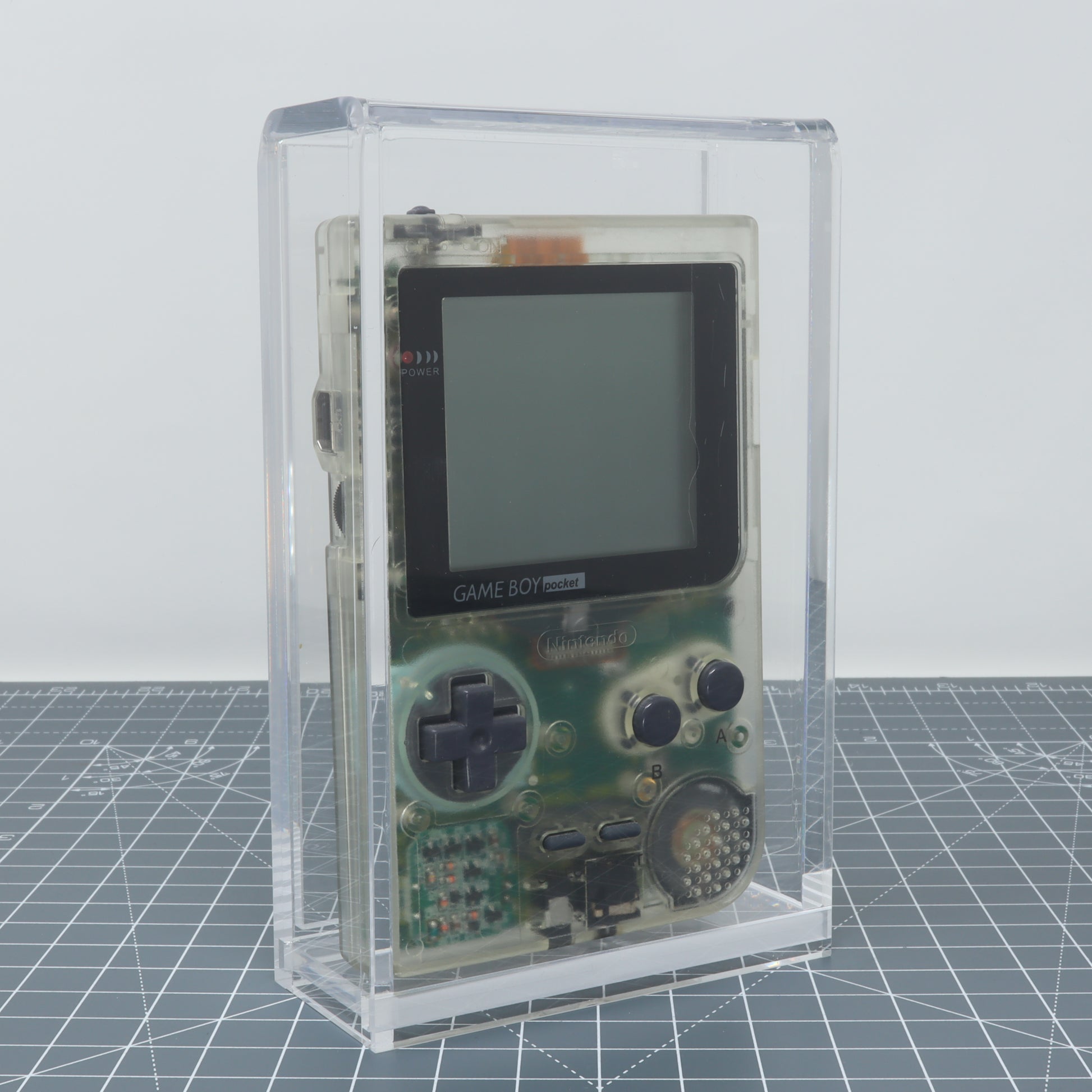 Transparent Game Boy Pocket encased in a clear acrylic display capsule for console protection.