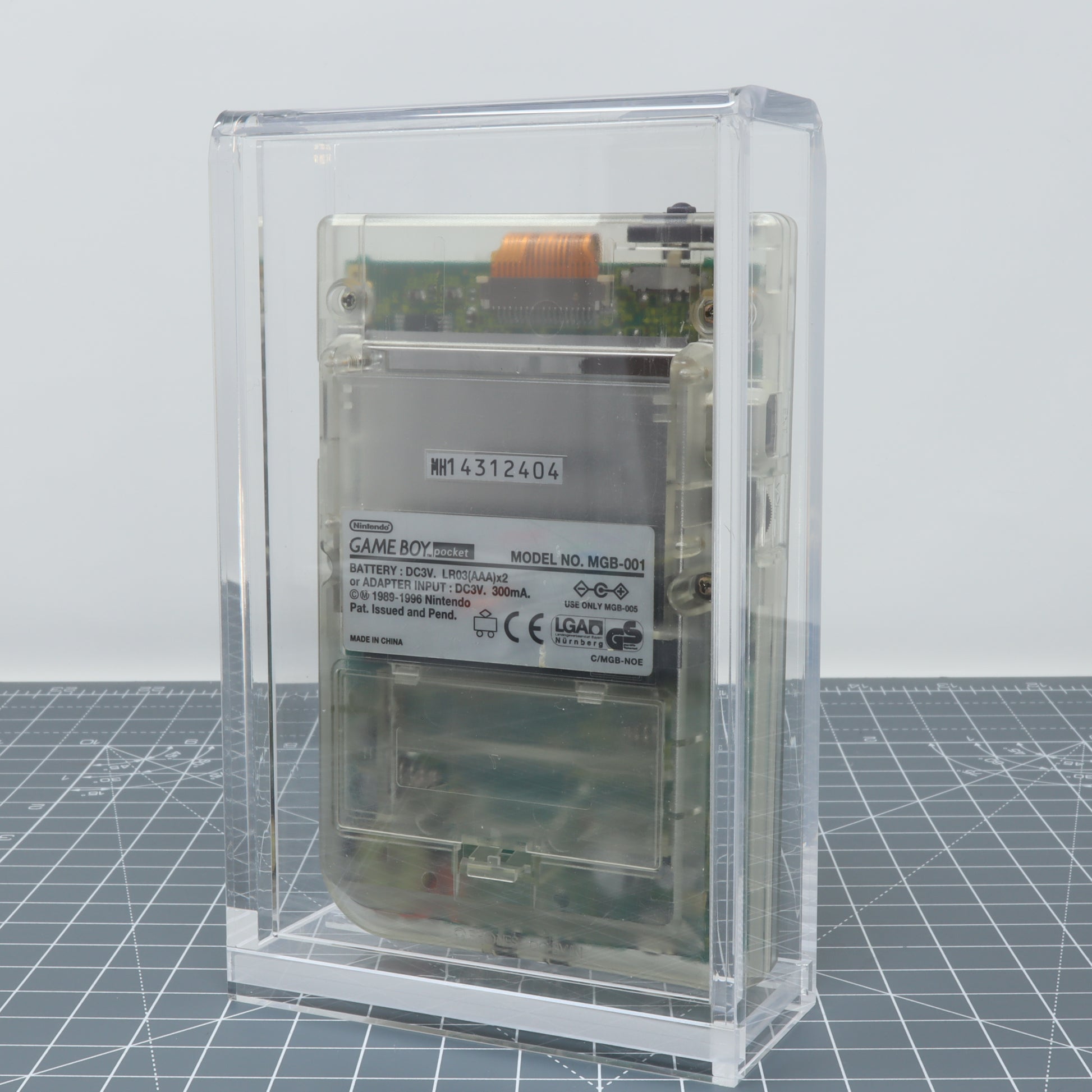 Transparent Game Boy Pocket encapsulated in a clear acrylic display capsule, displayed on a grid background.